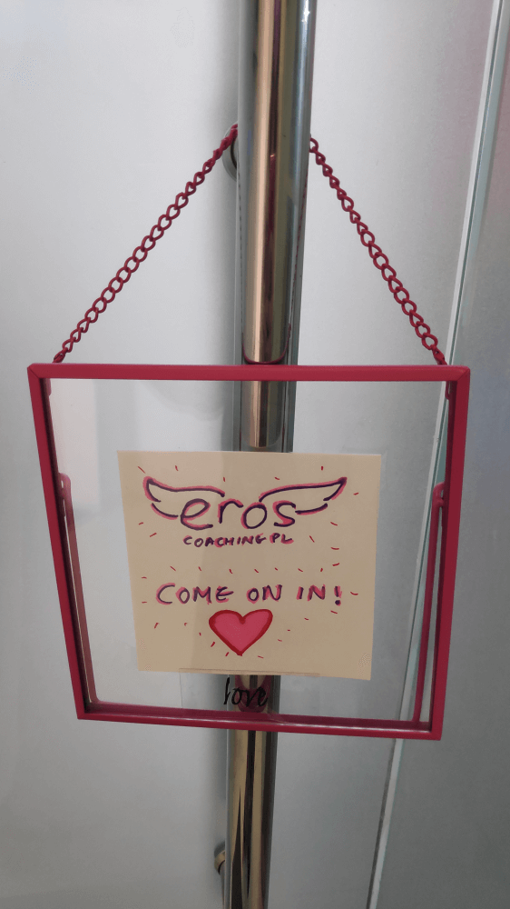 Hanging signage of Eros Coaching with come in text above the heart